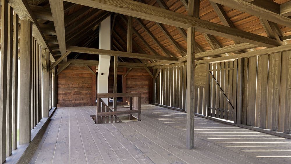 Ein leeres Holzgebäude mit offenem Innenraum, Holzbalken und Holzdielenboden.